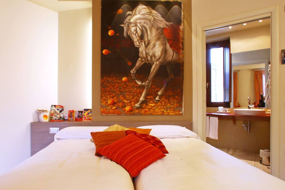 Een slaapkamer met een groot bed, een schilderij van een paard en een badkamer zichtbaar door een open deur.