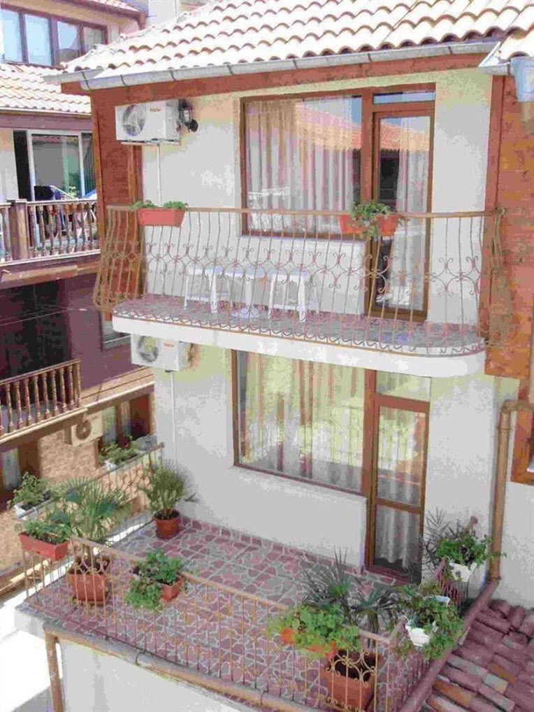 A two-story building with balconies, potted plants, and a tiled roof.