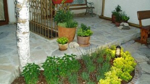 Une cour dallée de pierres, agrémentée de plantes en pot, d’un banc en bois et d’un portail en métal.