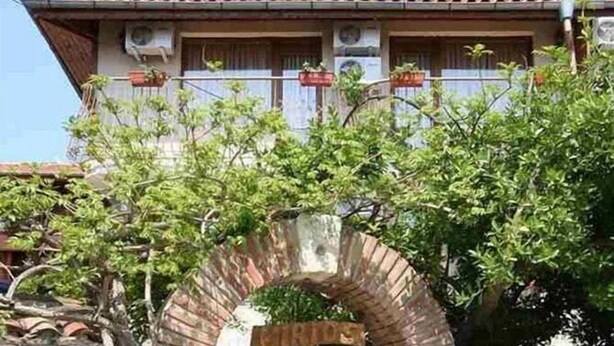 Un arc en pierre traditionnel qui mène à une porte en bois, avec une maison en arrière-plan.