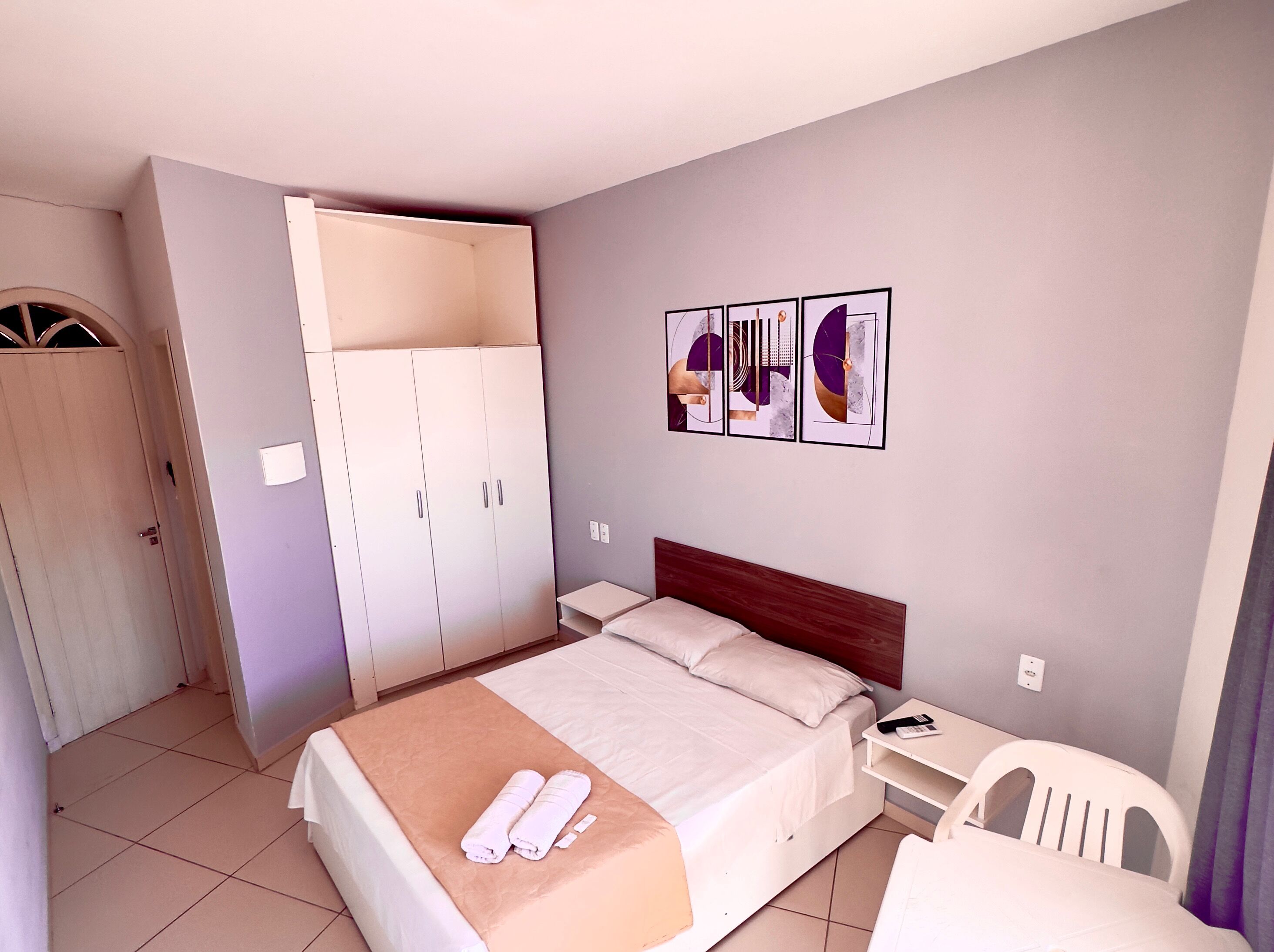 A hotel room with a bed, a wardrobe, a desk, and a chair.