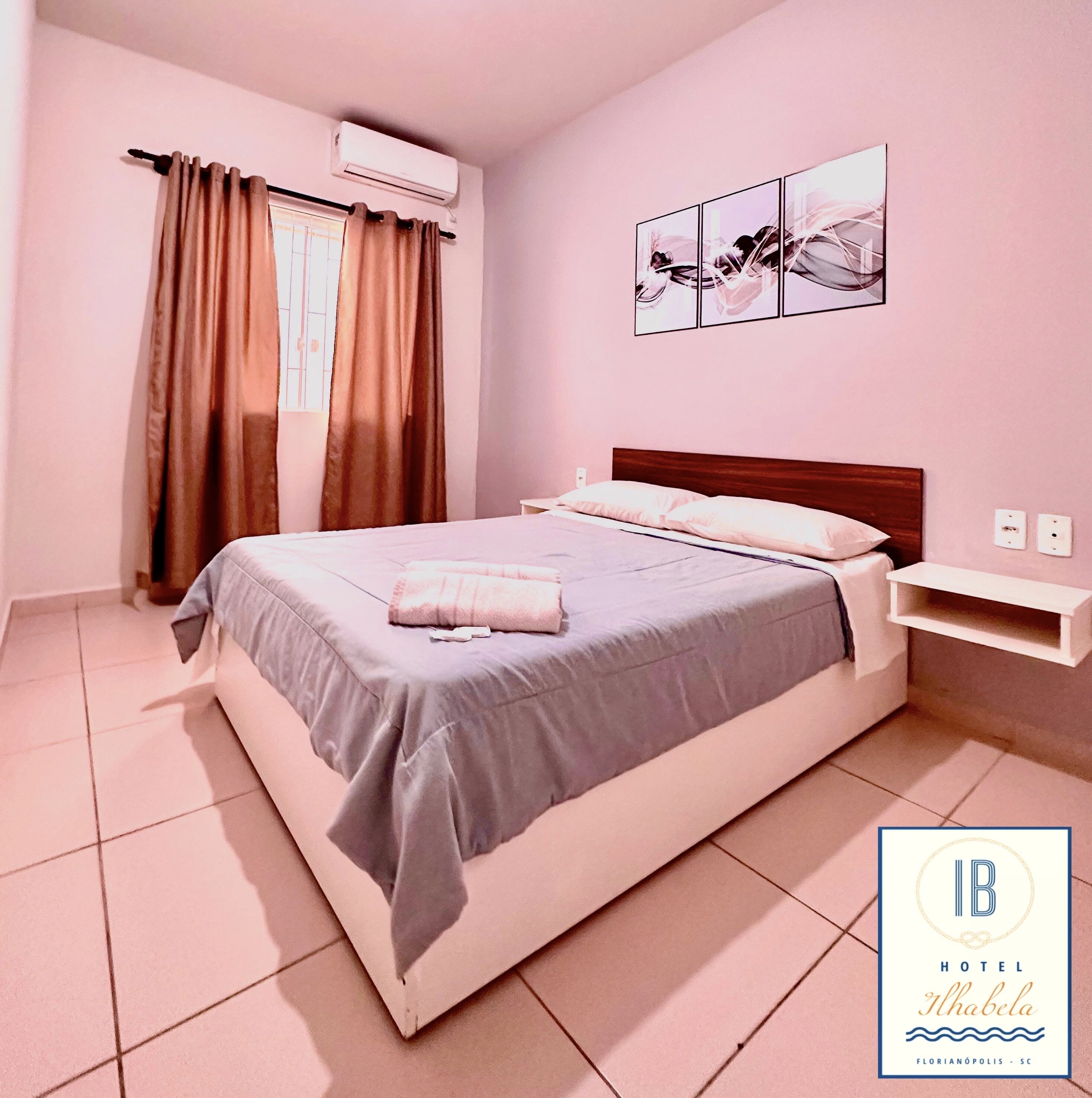 Un dormitorio con cama, cortinas, aire acondicionado instalado en la pared, mesita de noche y una obra de arte en la pared.