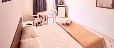 Habitación de hotel con cama, escritorio, silla, mesita, tetera y espejo.