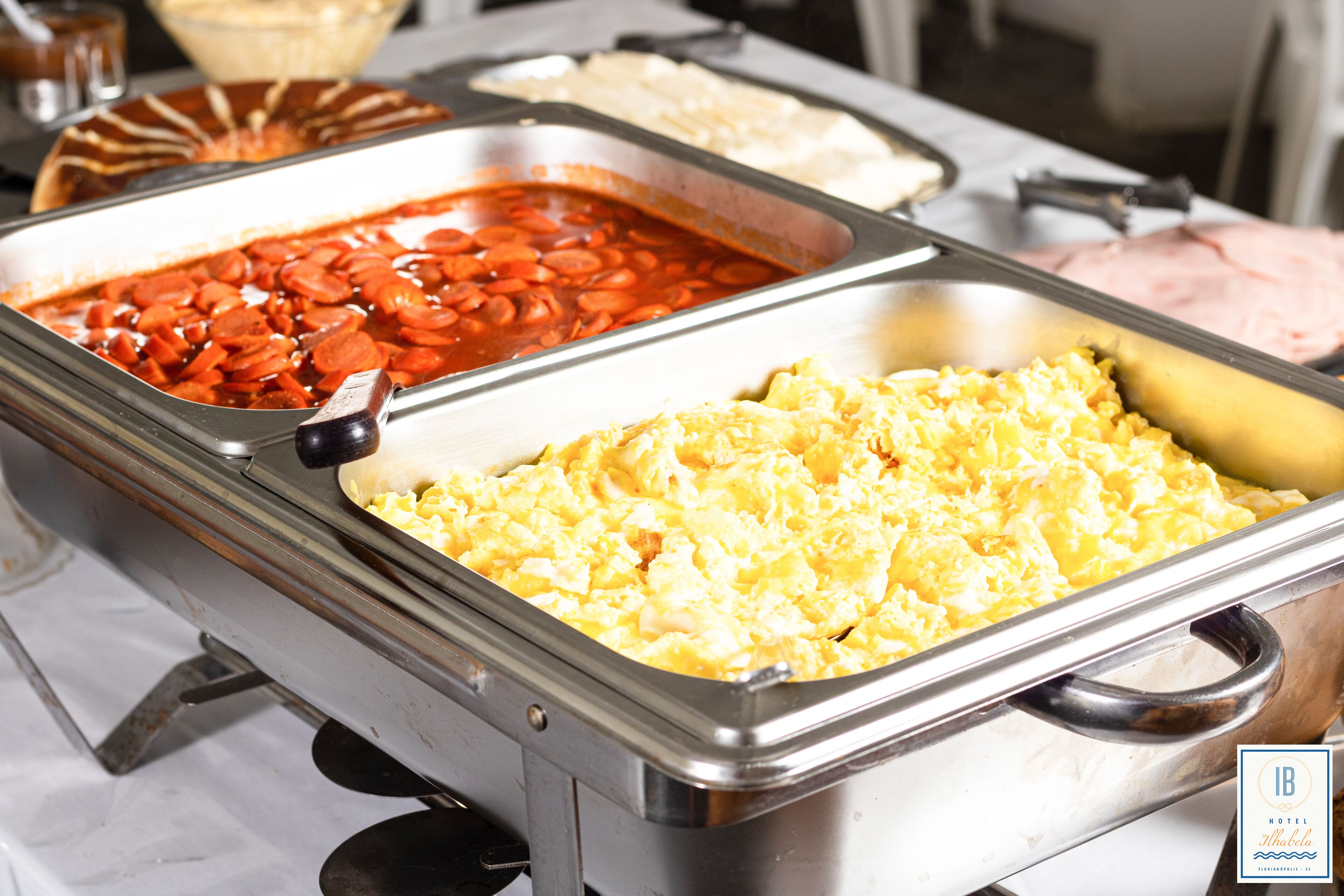 A buffet with various food options including scrambled eggs, beans, and sliced meats.