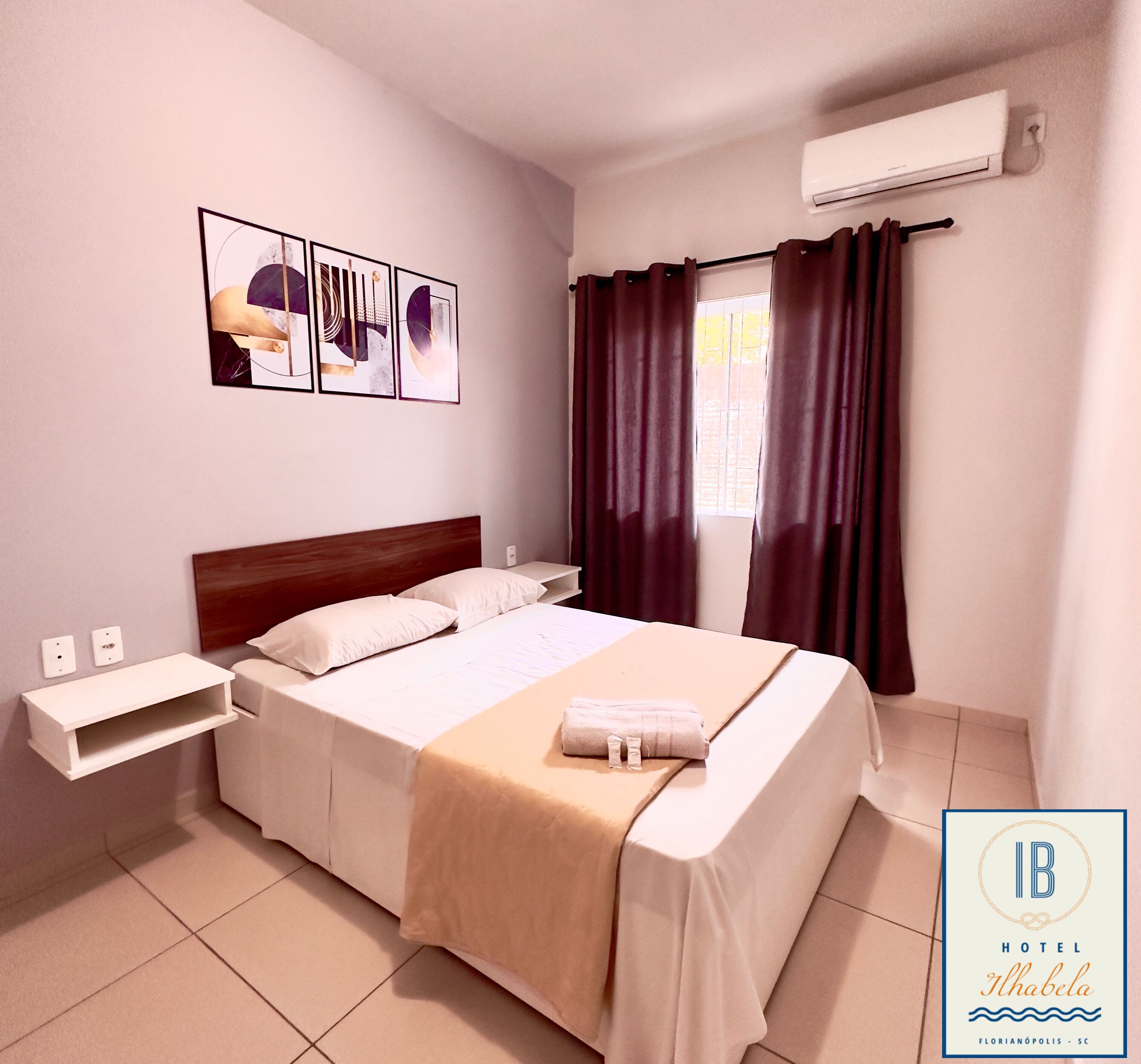 Habitación de hotel con cama, mesita de noche, aire acondicionado instalado en la pared y ventana con cortinas.