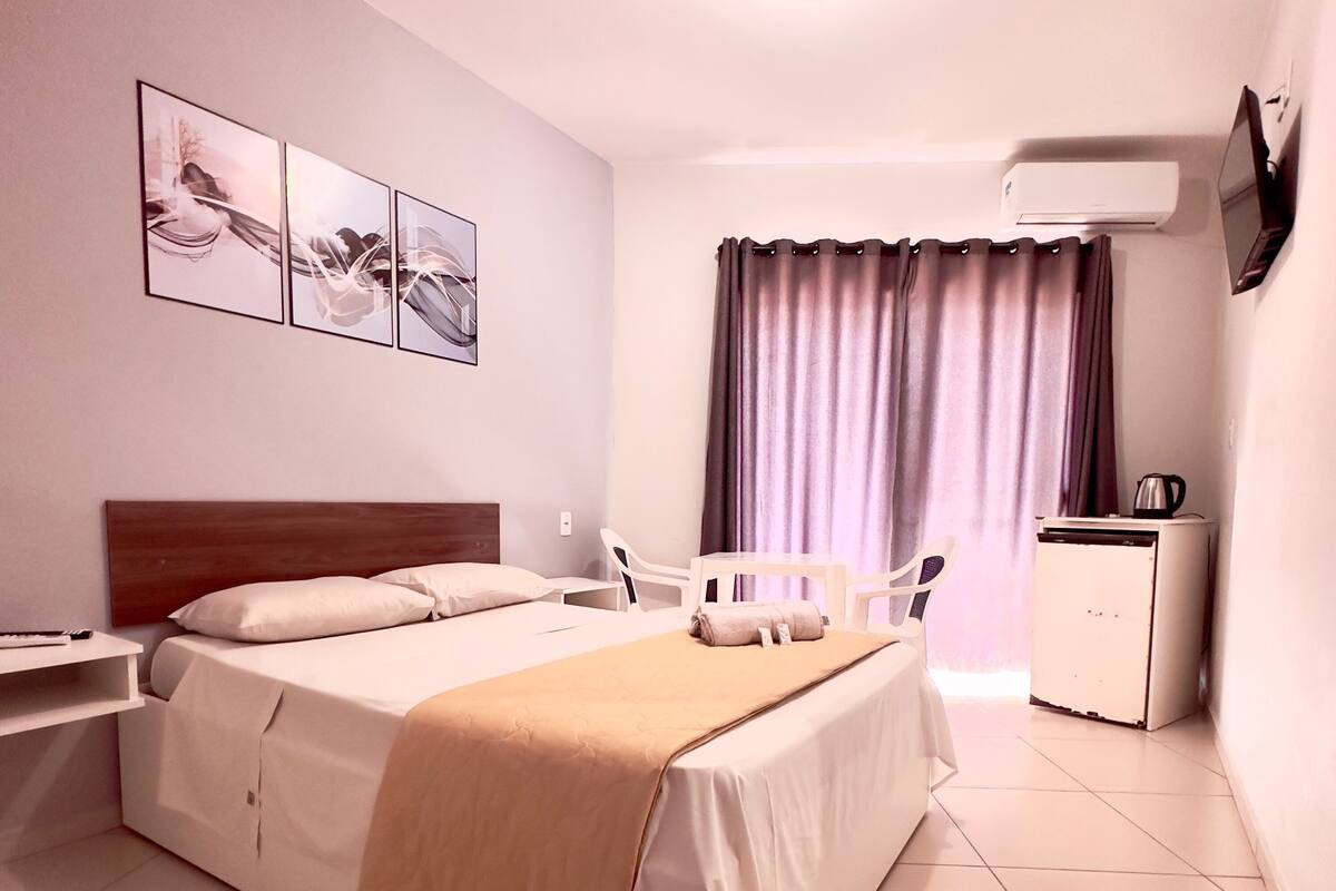 Habitación de hotel con cama, mesitas de noche, escritorio, silla, un mueble pequeño y televisión.