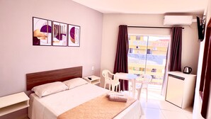 Habitación de hotel con cama, mesita de noche, un pequeño escritorio con silla, un mini refrigerador y vistas al exterior.