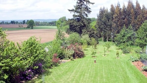 Un jardin bien entretenu, agrémenté de divers arbres et arbustes, une pelouse soigneusement taillée et une vue dégagée sur la campagne environnante.