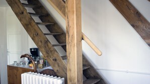 Un escalier en bois avec une rampe, un radiateur et un coin cuisine équipé de placards et d’appareils électroménagers.