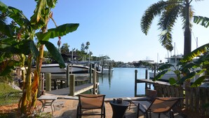 A waterfront patio with two chairs and a small table, overlooking a marina with boats and a dock.