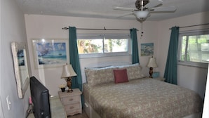 A bedroom with a bed, a TV, a desk, and a window with curtains.