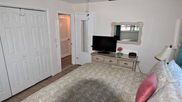 A bedroom with a bed, dresser, TV, and a door leading to another room.