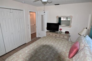 A bedroom with a bed, dresser, TV, and a door leading to another room.