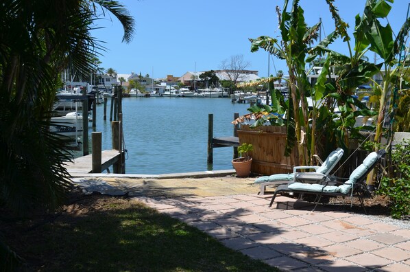 A marina with boats docked, a wooden dock, and a patio area with lounge chairs and a potted plant.
