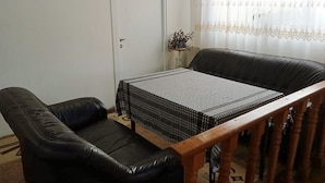 Um quarto com um sofá de couro preto, um banco de madeira e uma toalha de mesa quadriculada.