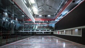 Una struttura sportiva interna con campo da tennis, zone relax e un soffitto alto con travi a vista.