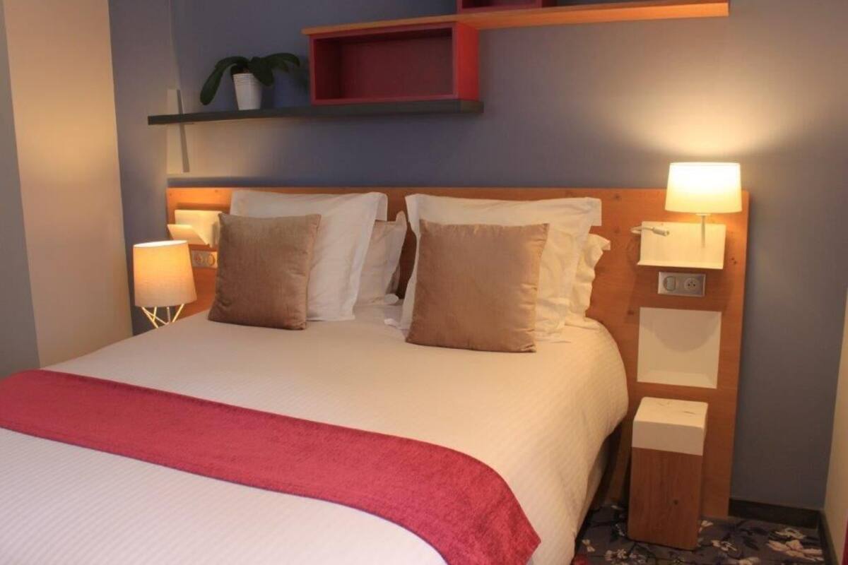 A neatly made bed with a red throw blanket, two bedside lamps, and a wooden headboard with shelves above.