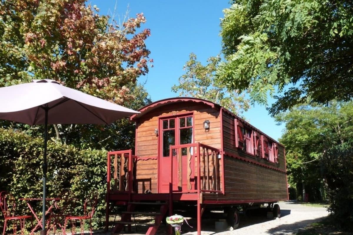 A wooden cabin with a porch, a table, and chairs, surrounded by trees.
