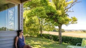 Una persona sentada en una terraza de madera con vistas a un árbol grande y un campo.