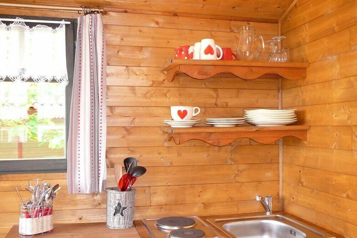 A wooden cabin kitchen with a sink, stove, and shelves holding cups and plates.