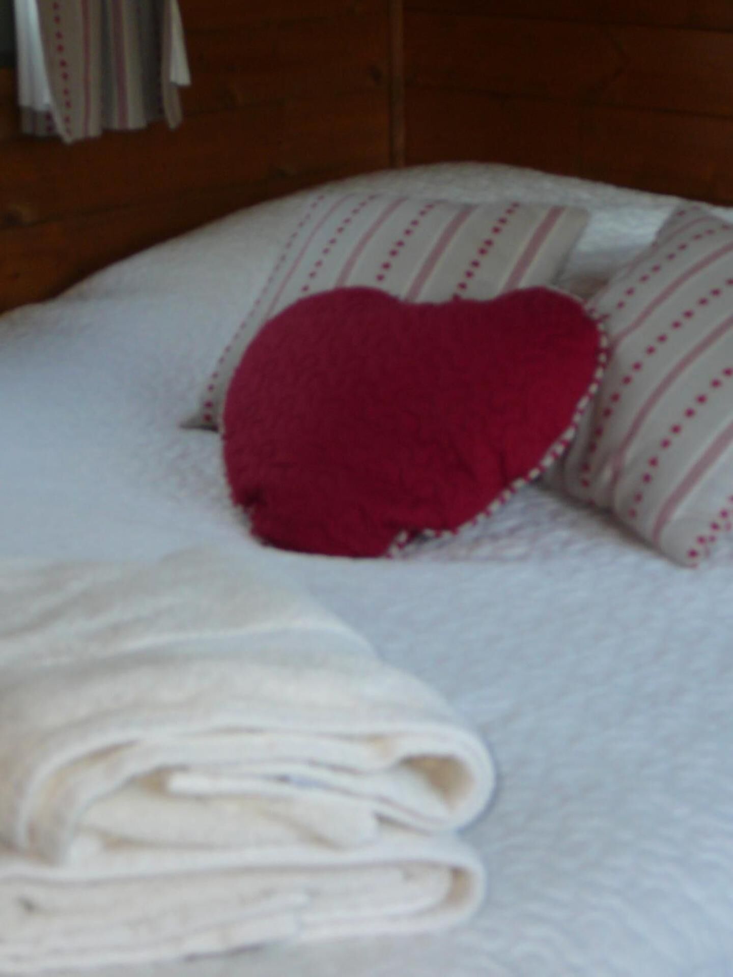 Een net opgemaakt bed met een hartvormig kussen en een gevouwen handdoek.