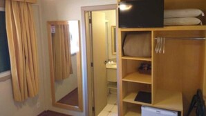 Ein Zimmer mit einem Holzschrank, einem darauf platzierten Fernseher, einem Spiegel und einer Tür zu einem weiteren Raum.