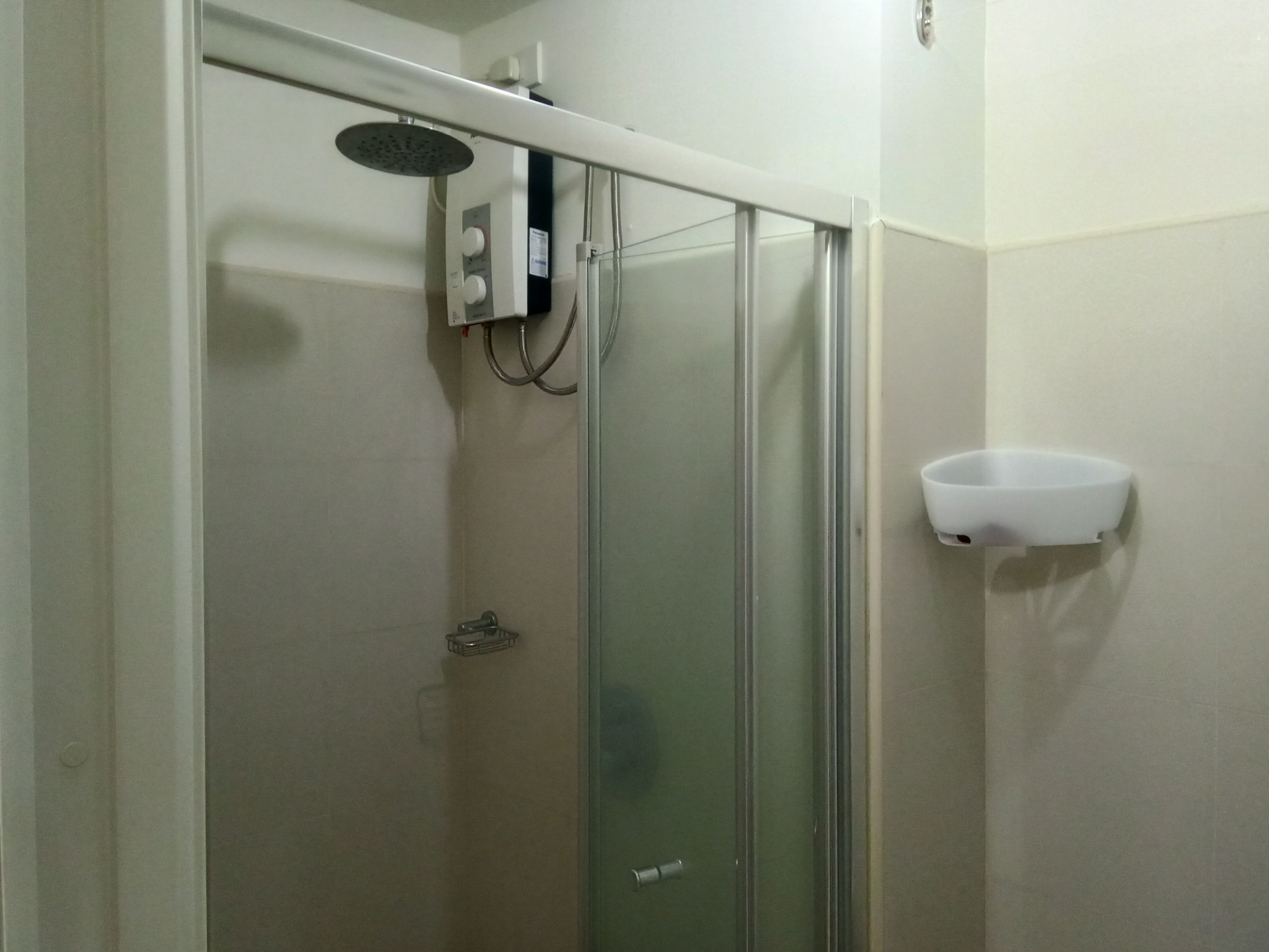 Ducha con puerta de vidrio, panel de control y lavamanos blanco.