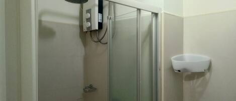 Ducha con puerta de vidrio, panel de control y lavamanos blanco.