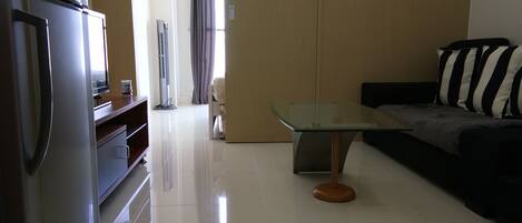 A modern living room with a glass-top coffee table, a sofa with striped cushions, and a built-in kitchen area with a refrigerator and a microwave.