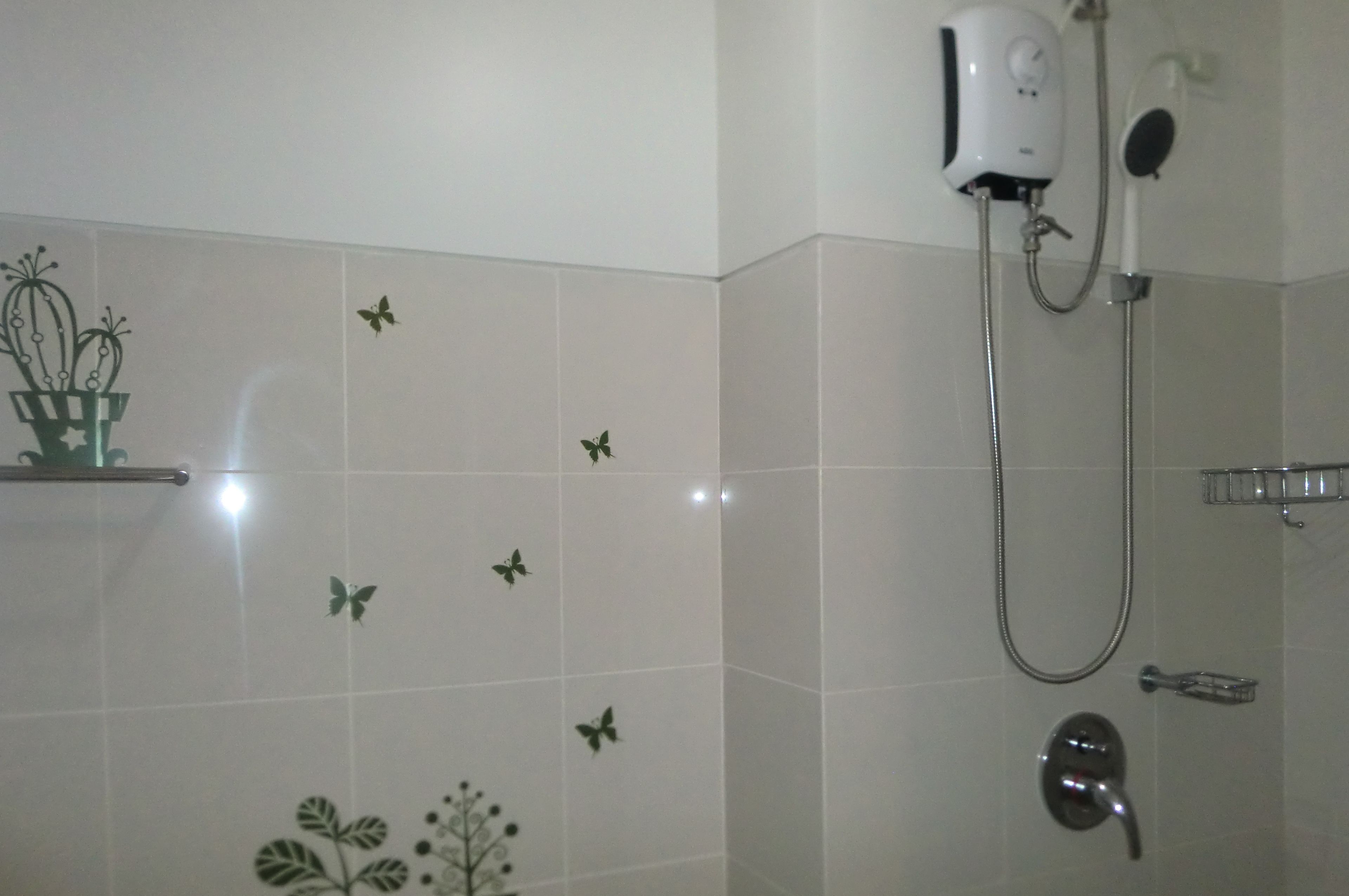 Un baño con ducha, secador de manos y azulejos decorativos con diseños de mariposas.