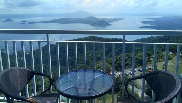 A balcony with two chairs and a glass table overlooking a scenic view of a bay with islands and a mountain range.