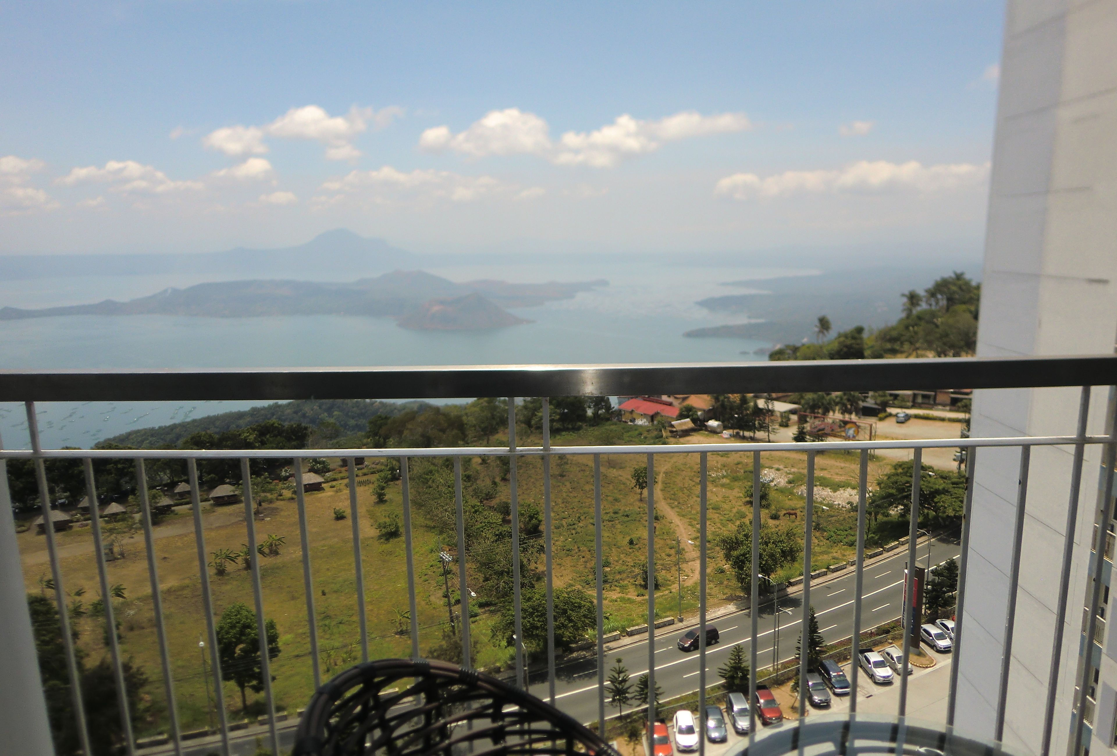 A balcony with a view of a road, parked cars, and distant islands.