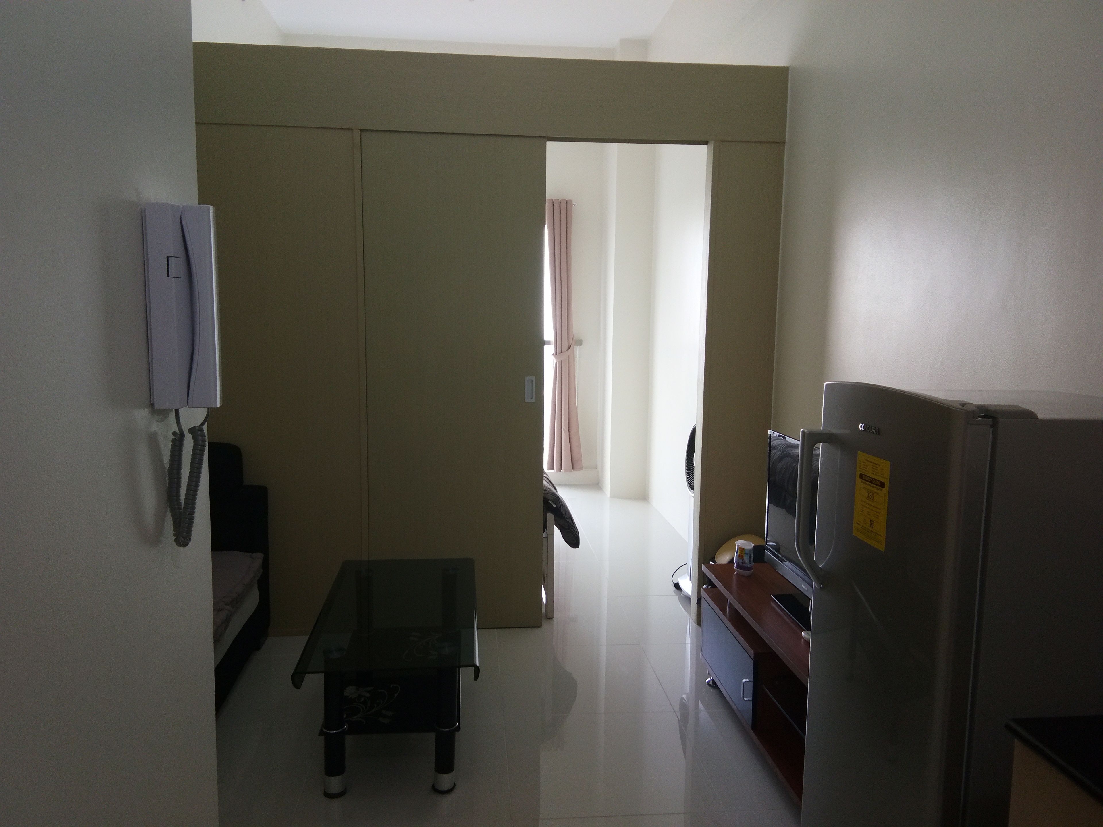A compact kitchen with a refrigerator, a small table, and a telephone.
