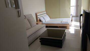 Una habitación moderna con sofá, cama, televisor y una mesa de centro de vidrio.