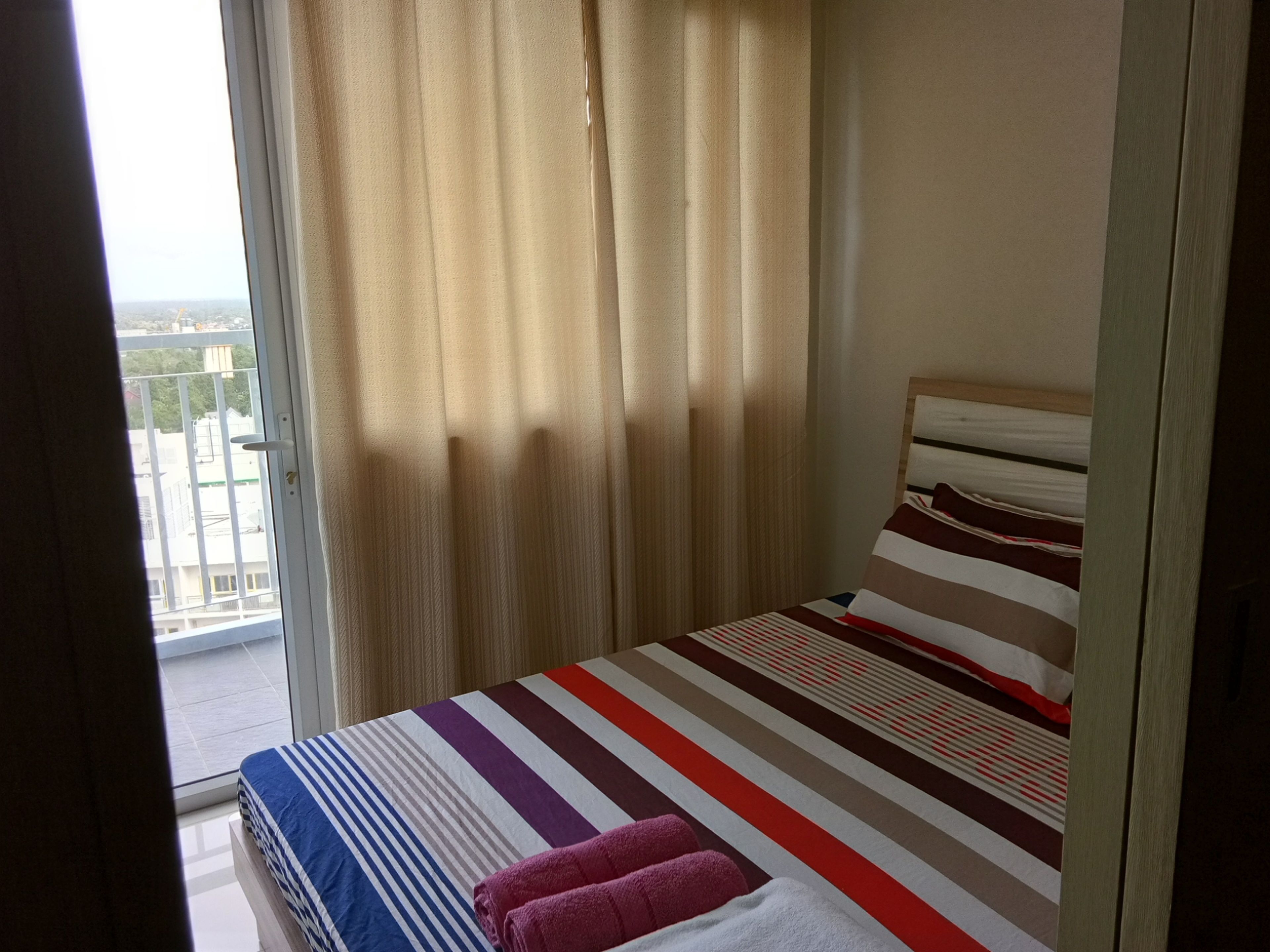 A bedroom with a bed, curtains, and a view of buildings outside.