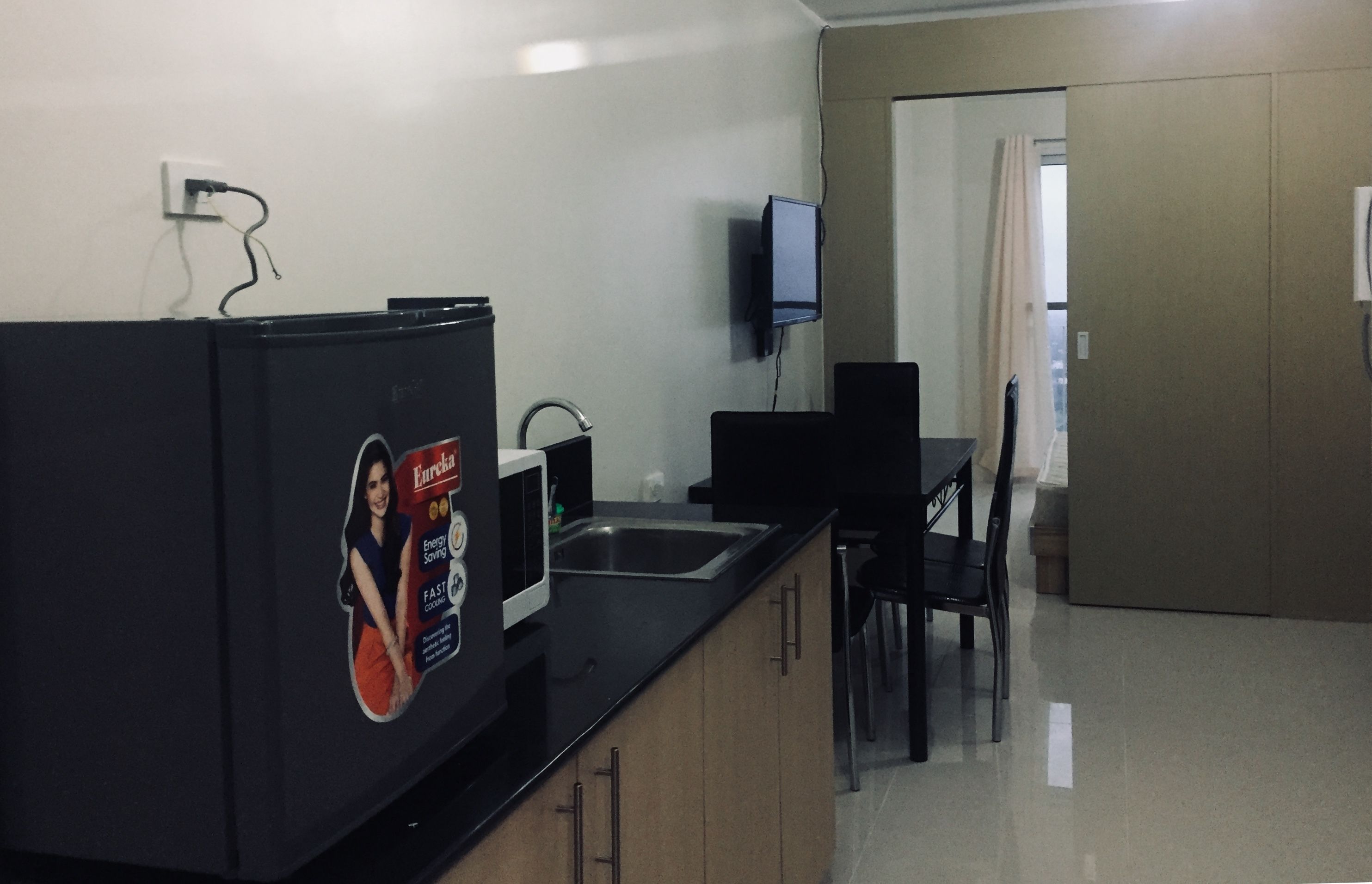Cocina compacta con refrigerador, lavamanos y televisor de pantalla plana montado en la pared.
