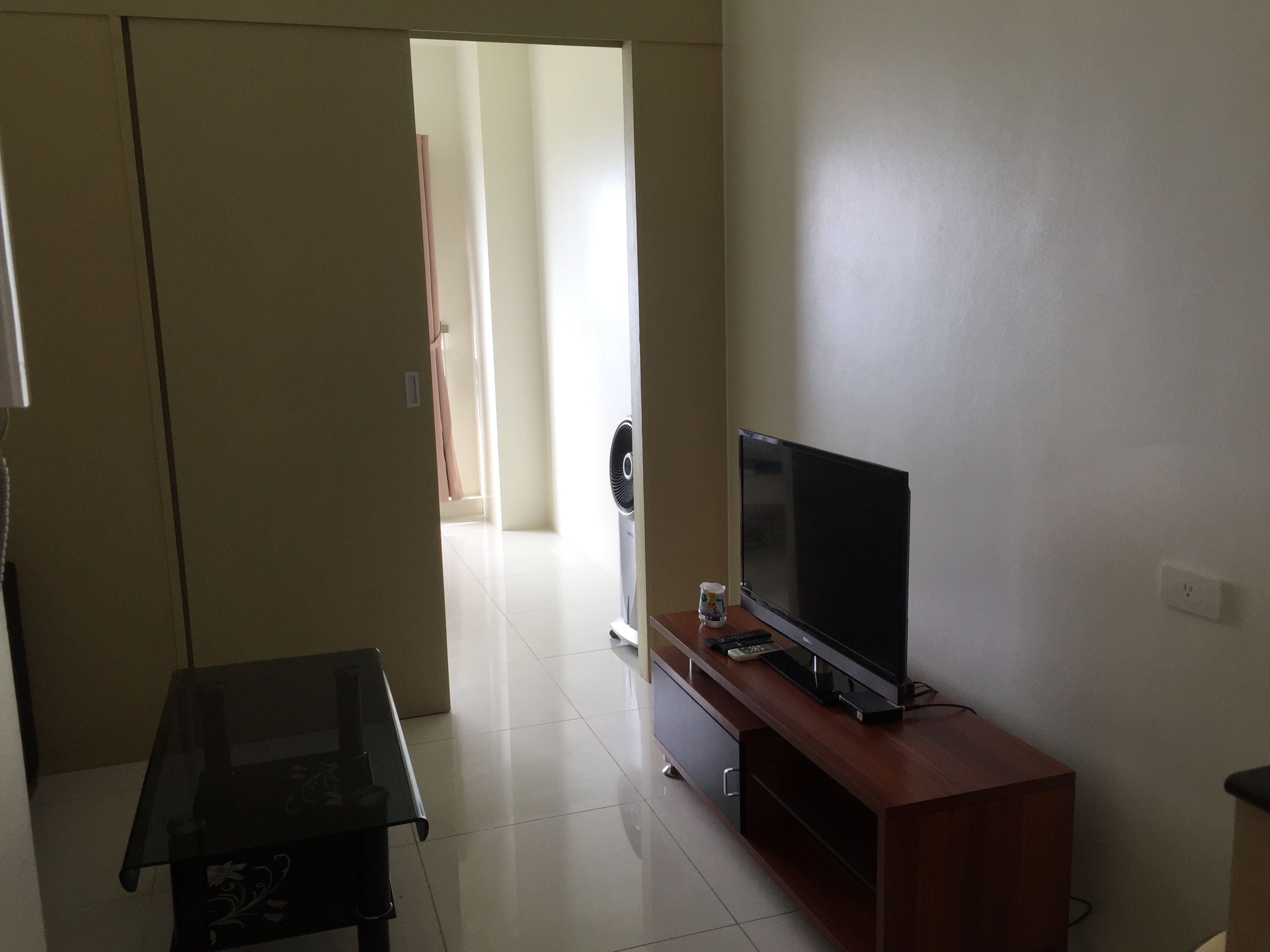 Una sala de estar con una televisión de pantalla plana sobre un soporte de madera, una mesa de centro de vidrio y una puerta que da a otra habitación.