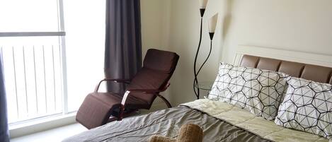 A hotel room with a bed, a chair, a window with curtains, and a bedside lamp.