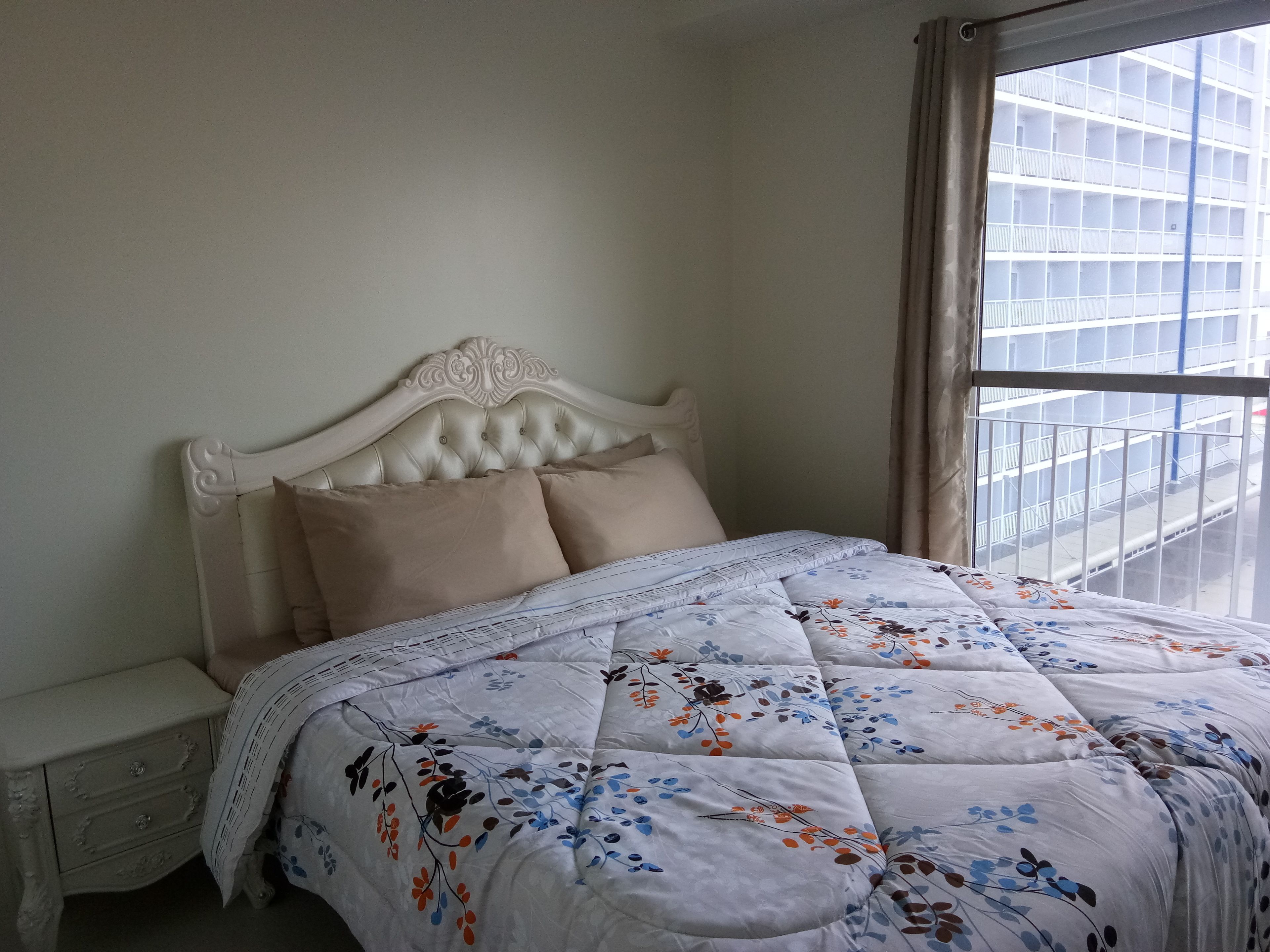 A neatly made bed with a floral quilt, a white headboard, and a nightstand with a drawer.