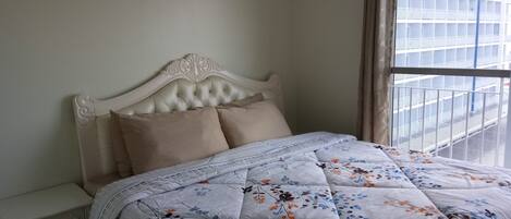 Una cama bien tendida con un colcha floral, un cabecero blanco y una mesita de noche con cajón.