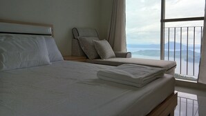 A hotel room with a large bed, a chair, and a view of mountains through a balcony.