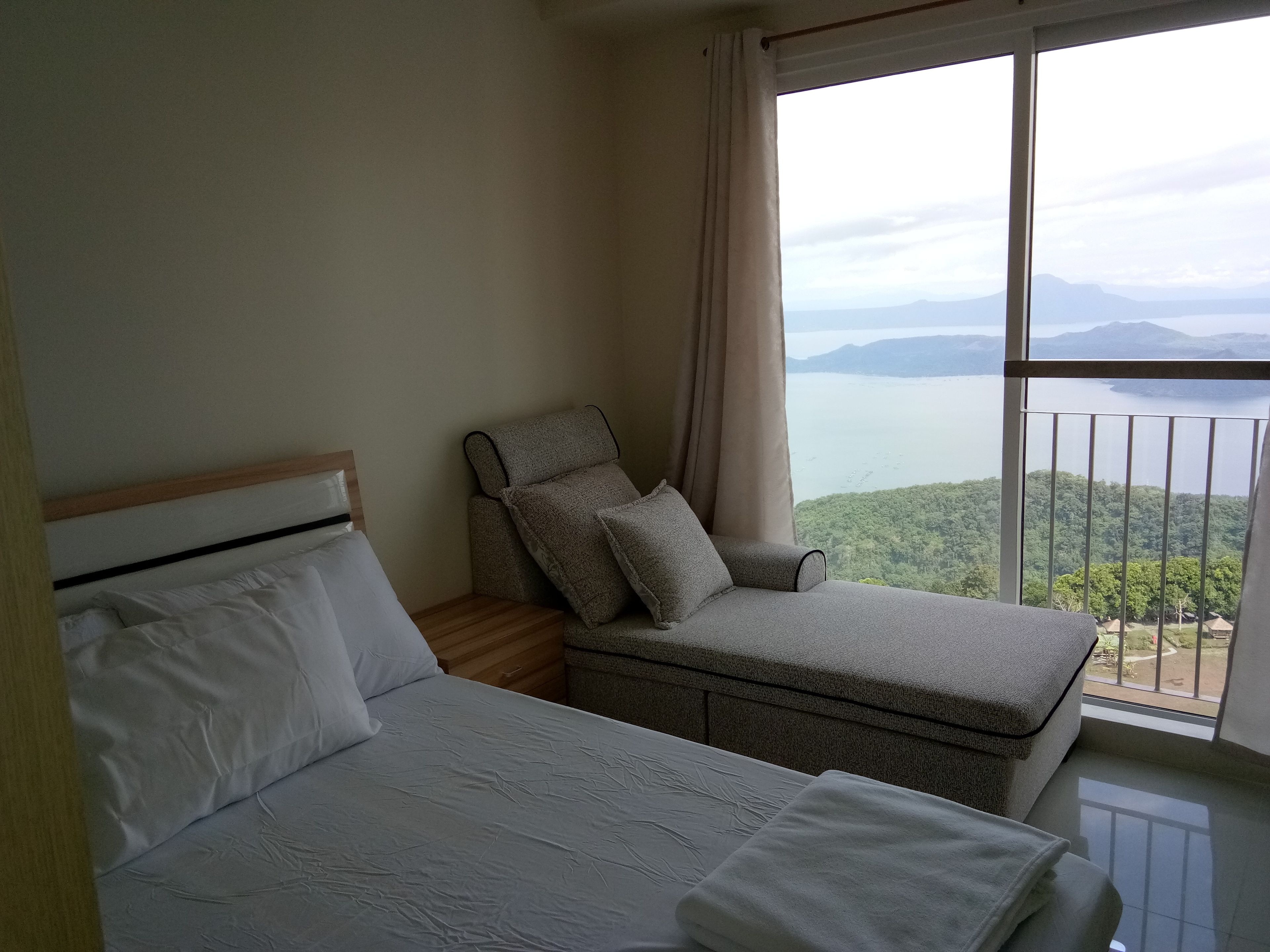 Ein Schlafzimmer mit einem Bett, einem grauen Sessel und einem großen Fenster mit Blick auf einen See und Berge.