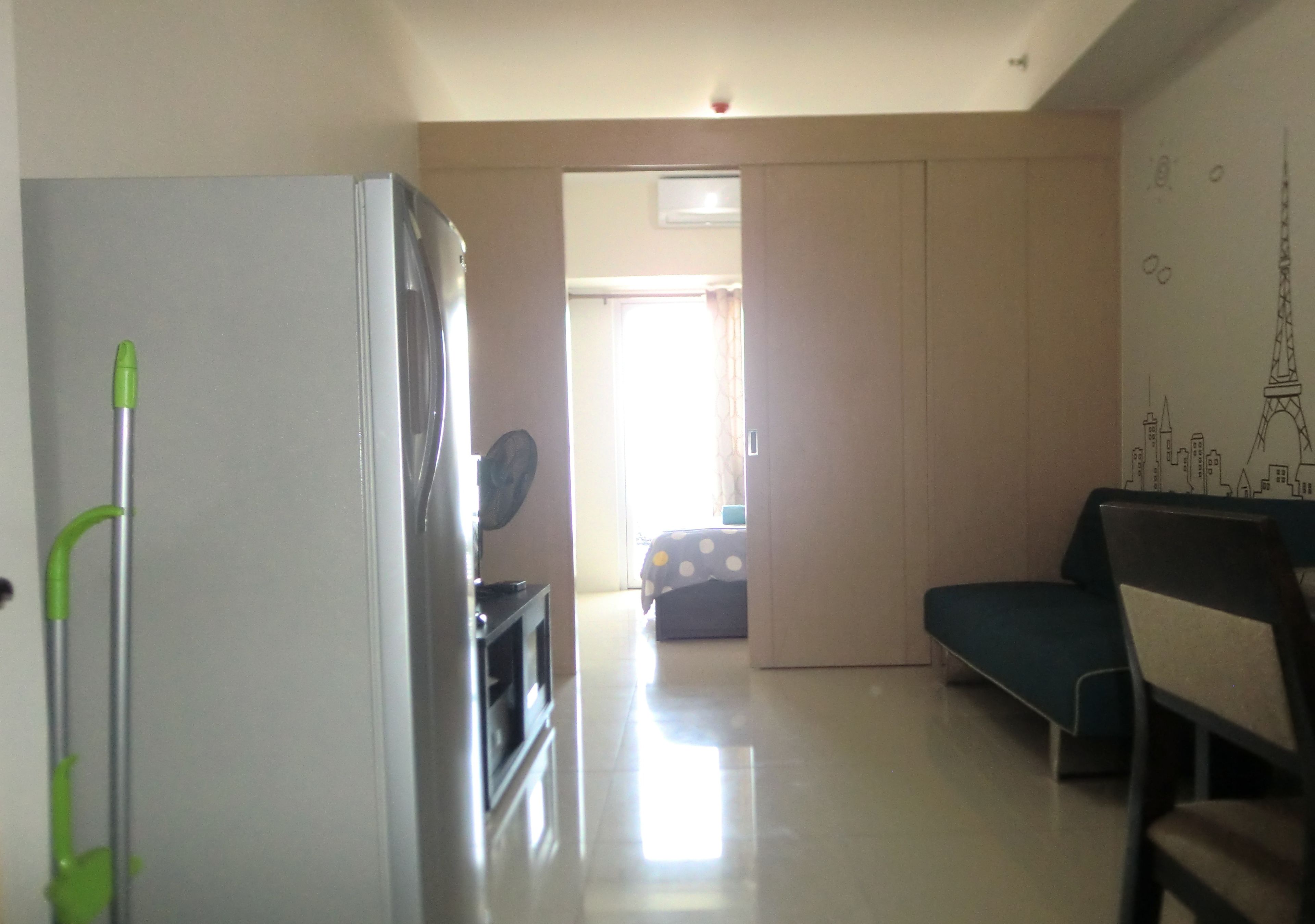 A living room with a sofa, a dining table, and a refrigerator. There is a hallway leading to another room.