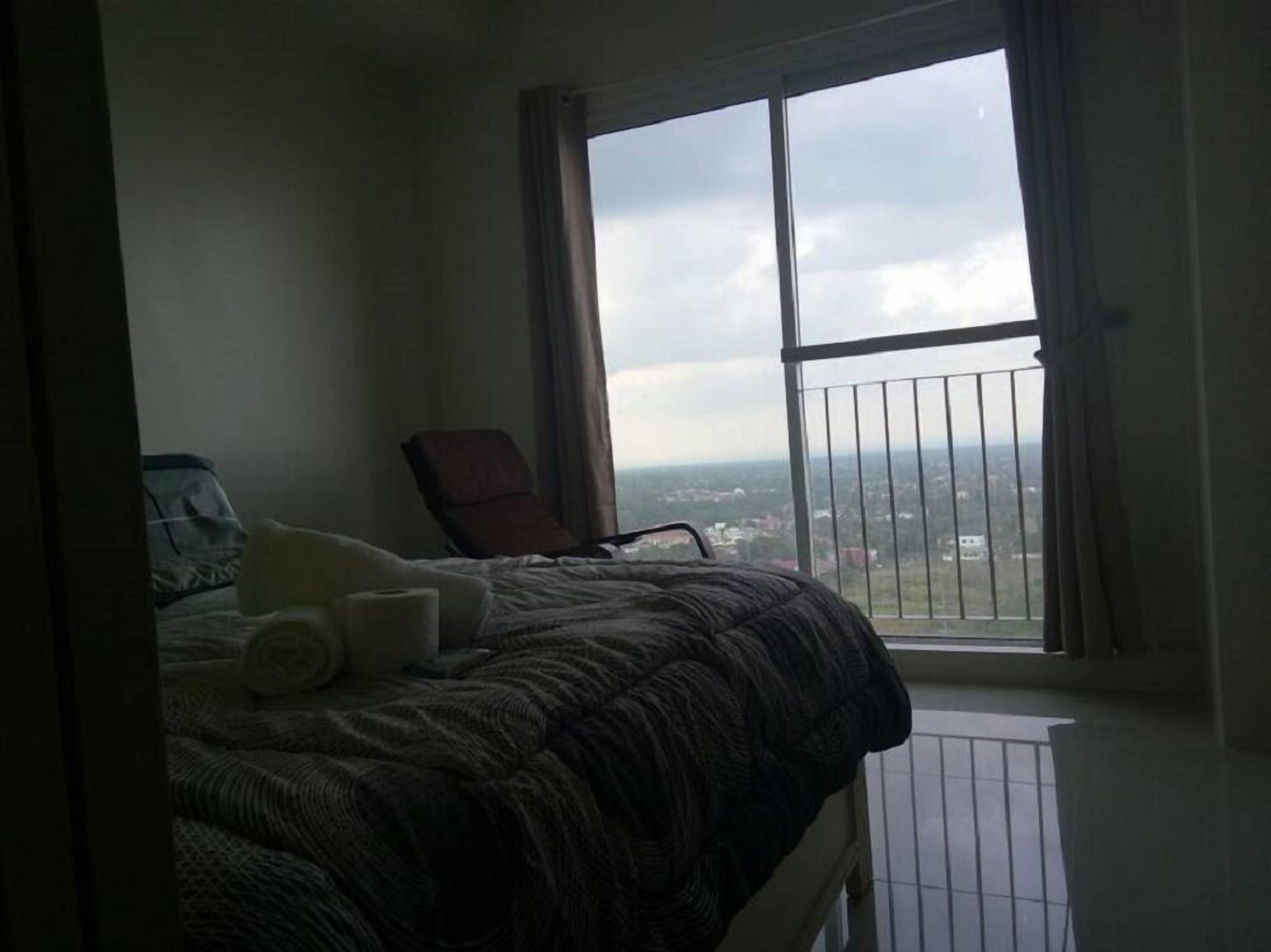 Un dormitorio con un ventanal grande, una cama, una silla y vistas a la ciudad.