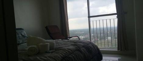 Un dormitorio con un ventanal grande, una cama, una silla y vistas a la ciudad.