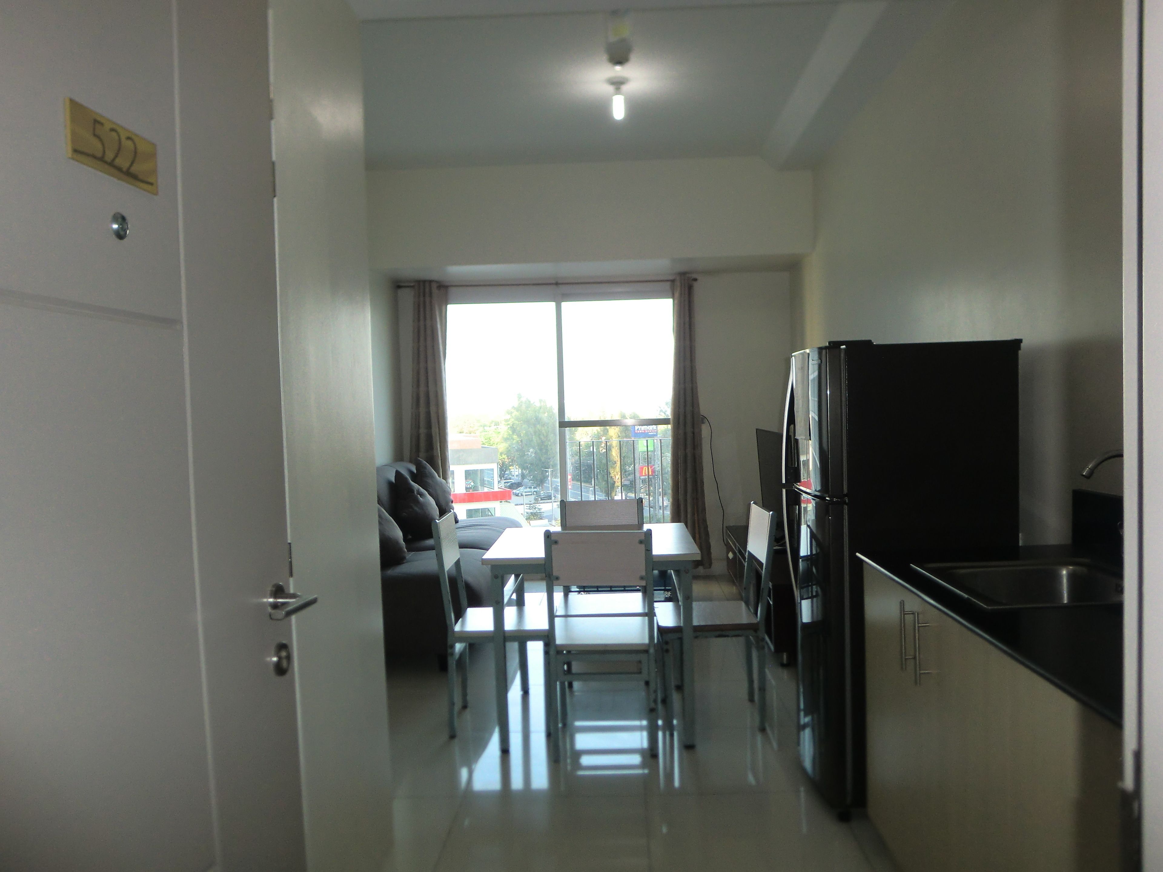 A modern kitchen with a dining area, a refrigerator, and a view through a large window.