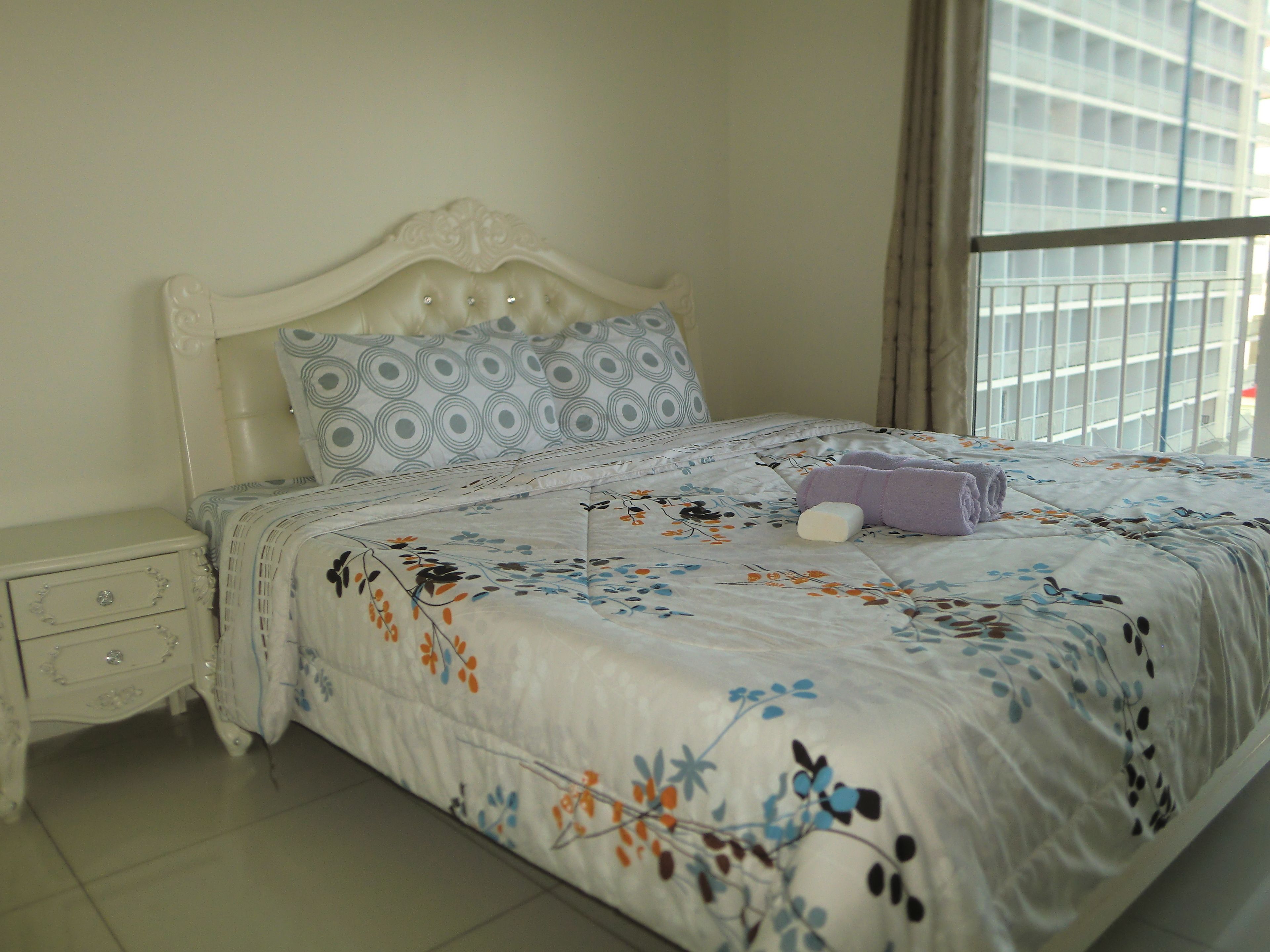 A neatly made bed with floral bedding, a white headboard, and a nightstand with drawers.