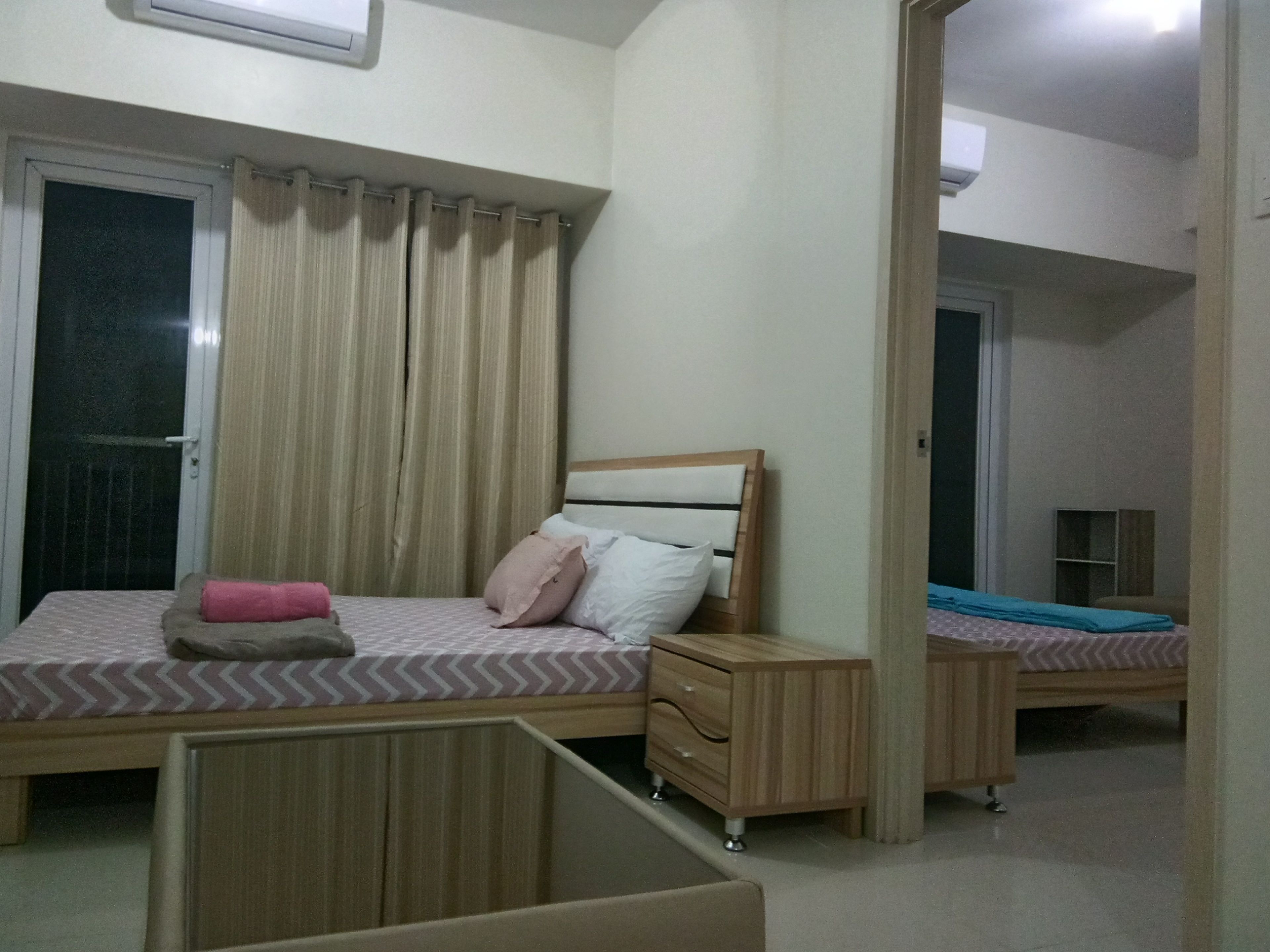 A bedroom with a bed, a nightstand, a dresser, and a window with curtains.