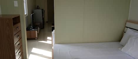 A hotel room with a bed, a wooden dresser, a television, and a desk.