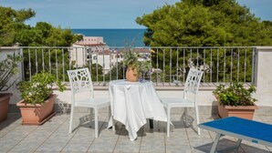 A terrace with a table and chairs, potted plants, and a view of the sea. - Hotel Pineta (Vico del Gargano)